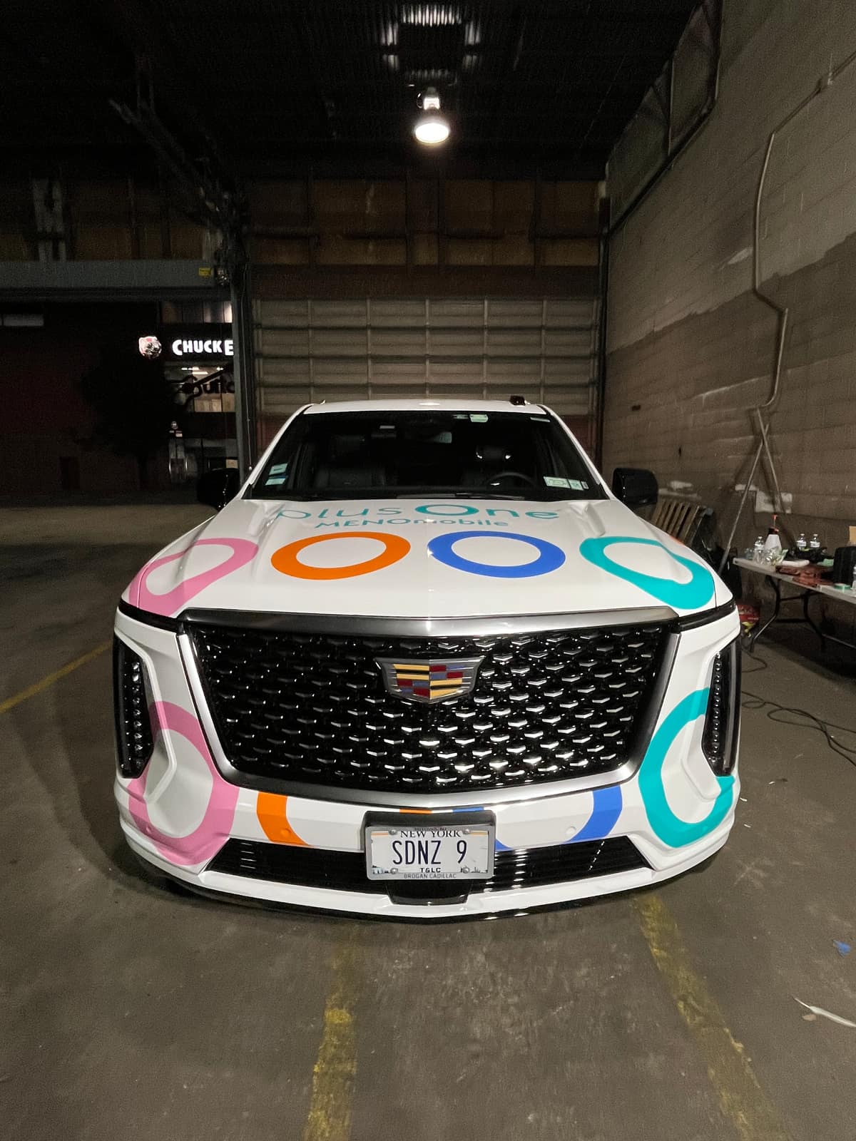 White Cadillac Escalade with a multicolor plusOne ring wrap, front view inside the shop