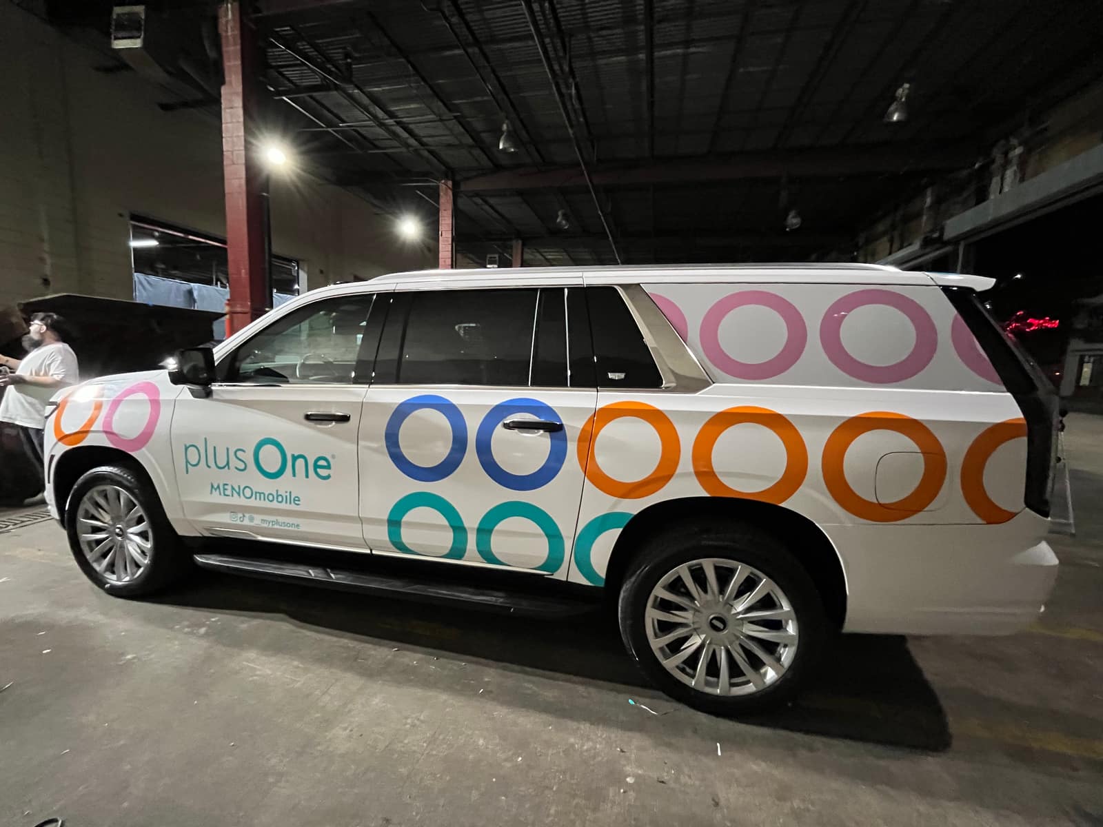 White Cadillac Escalade with multicolor plusOne ring graphics, side view in the wrap shop