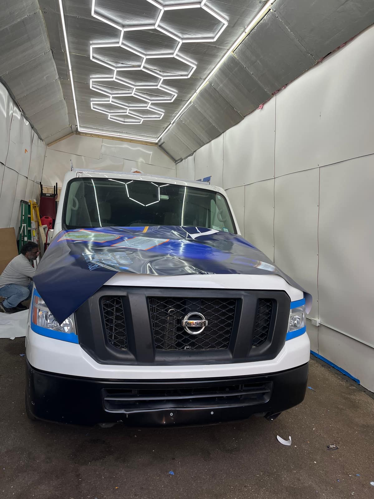 Nissan NV partway through a wrap, with blue printed film on the hood and front while the rest of the body is still white