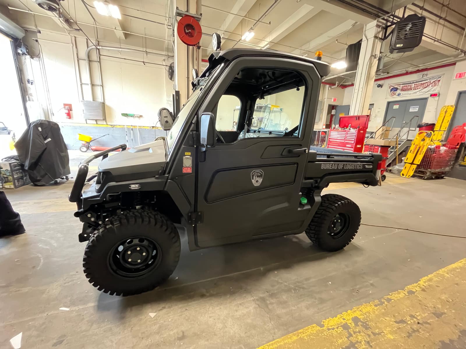 Dark green FDNY utility vehicle with a cab, viewed from the side inside a garage