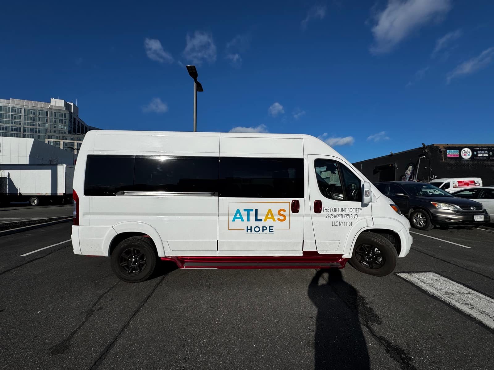 White Ram ProMaster passenger van for Atlas Hope with a small logo and partial graphics, parked outdoors