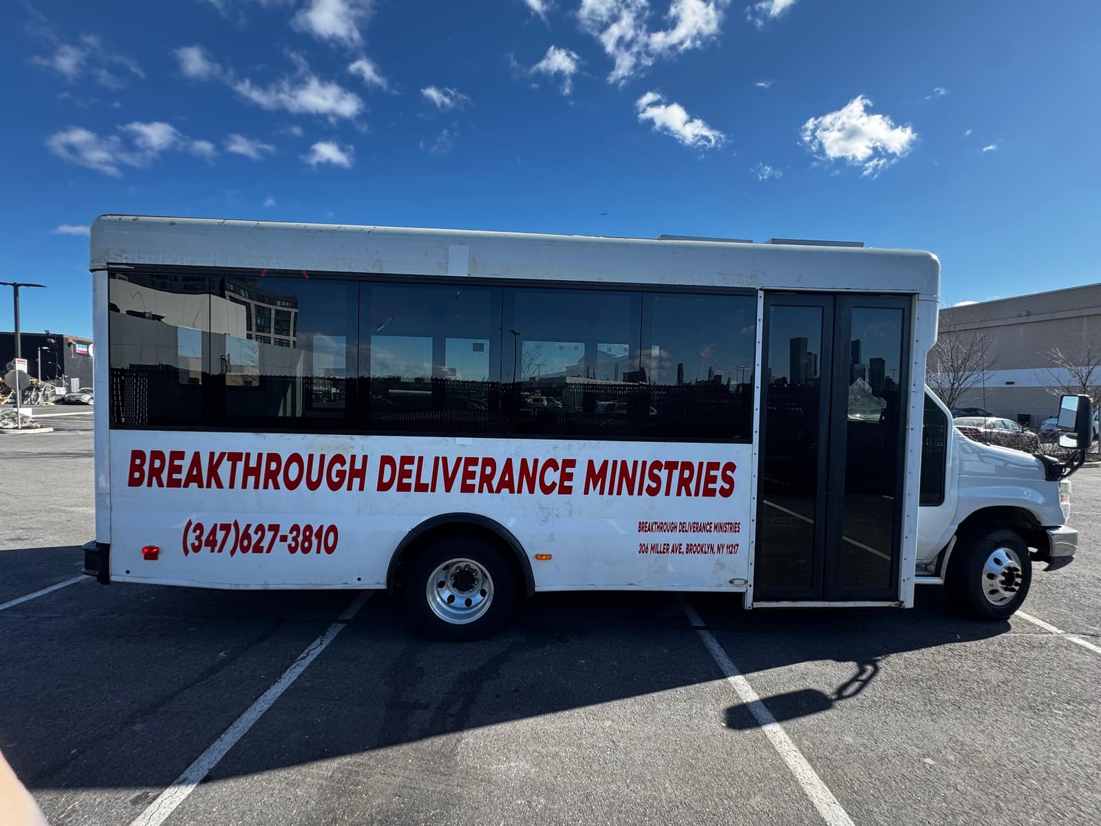 White shuttle bus outdoors with red cut vinyl lettering reading Breakthrough Deliverance Ministries and a phone number