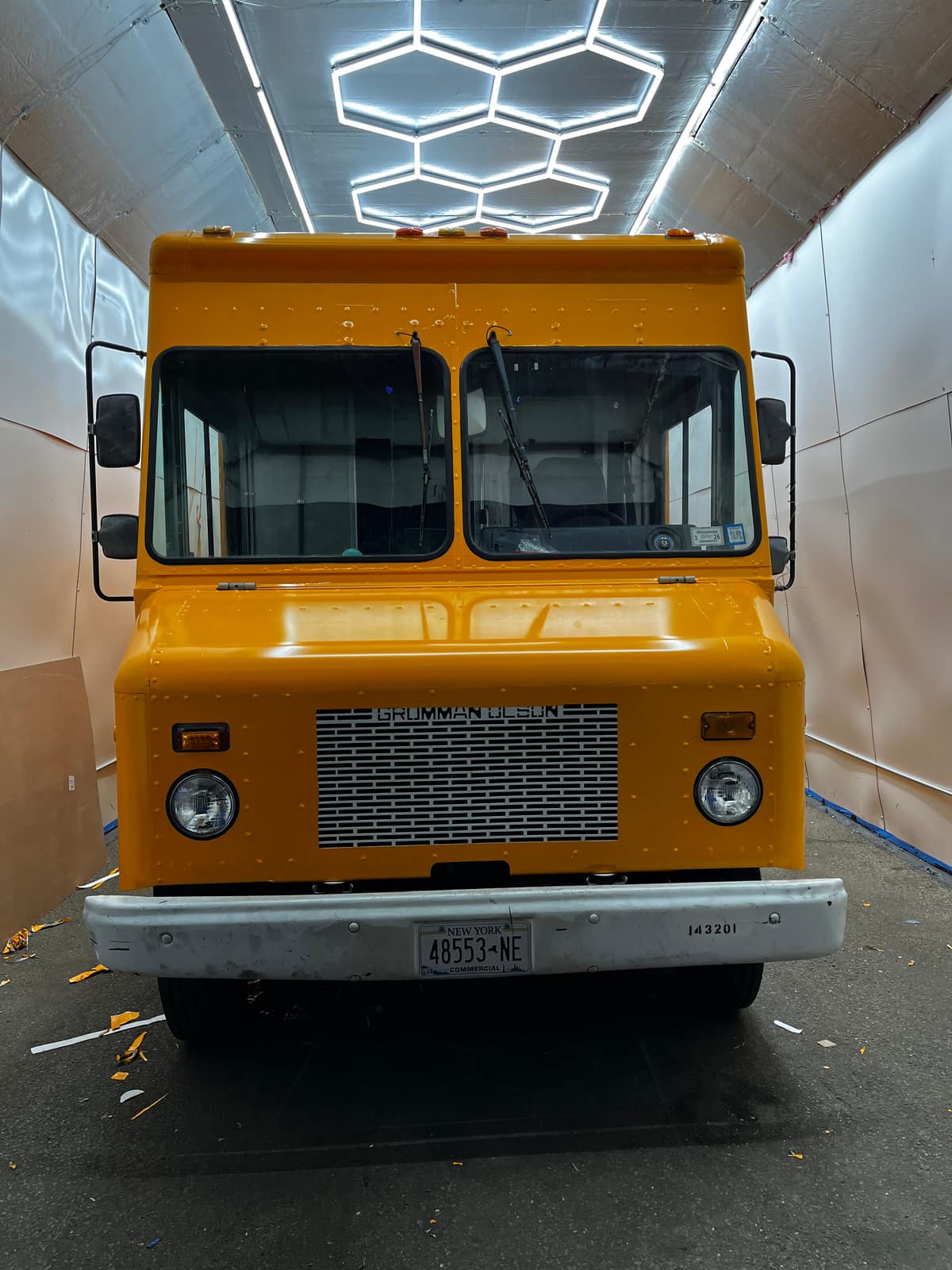 Front of an orange step van in the wrap shop under hexagon ceiling lights