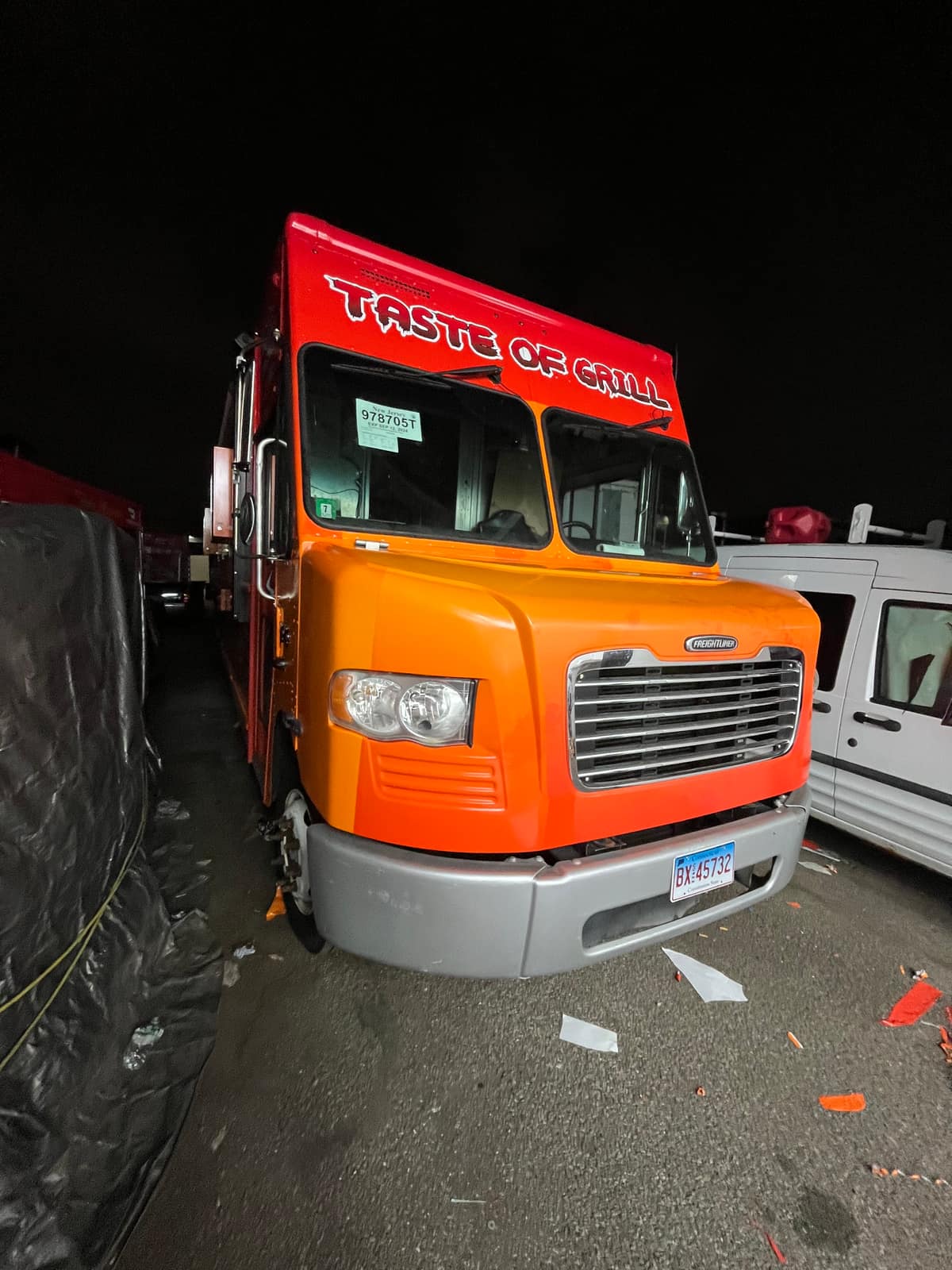 Front three-quarter view of the Taste of Grill food truck at night in the lot with the cab wrapped