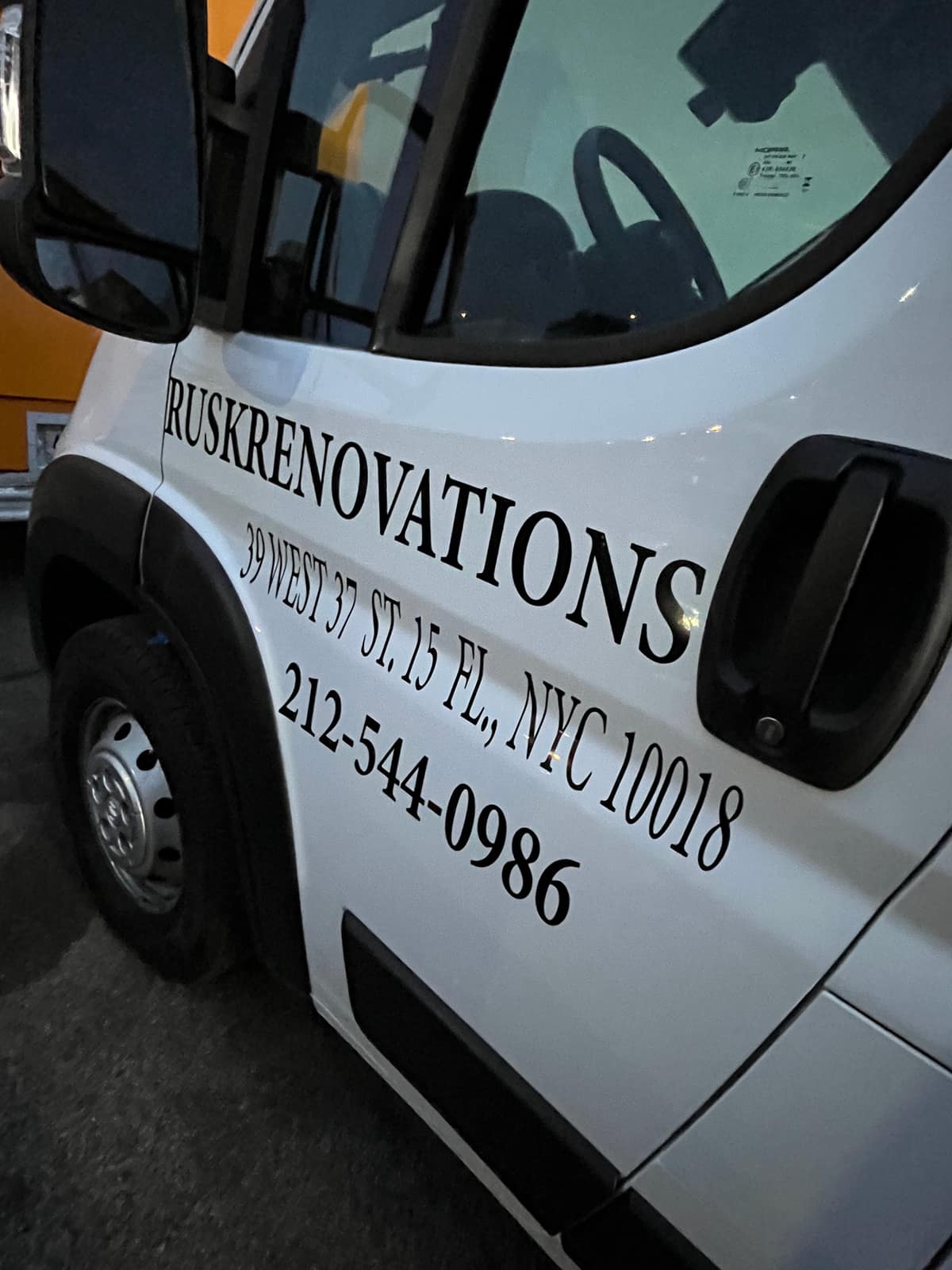 Close-up of white van door lettering reading Rusk Renovations, 39 West 37 St, NYC 10018, with a phone number