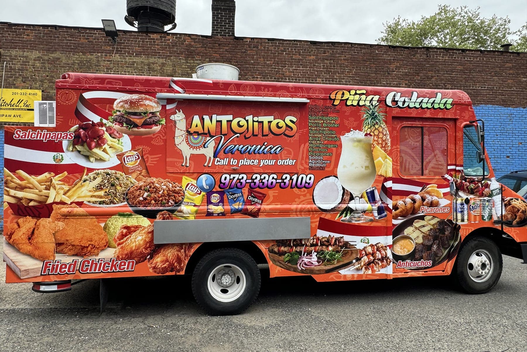 Red Antojitos Veronica food truck with printed food photography and a 973 phone number, side view