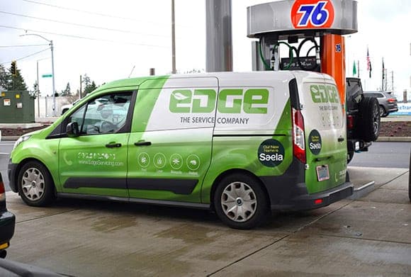 Green Ford Transit Connect in a printed wrap for Edge The Service Company, parked at a gas station