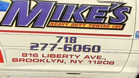 Close-up of the Mike's Heavy Duty Towing door lettering: purple logo, 718 phone number and Liberty Ave, Brooklyn NY 11208 address