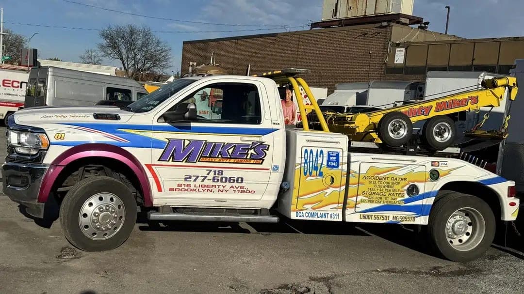 White Ram tow truck for Mike's Heavy Duty Towing, a Brooklyn towing company, with purple, blue and yellow graphics and door lettering, side view in a yard