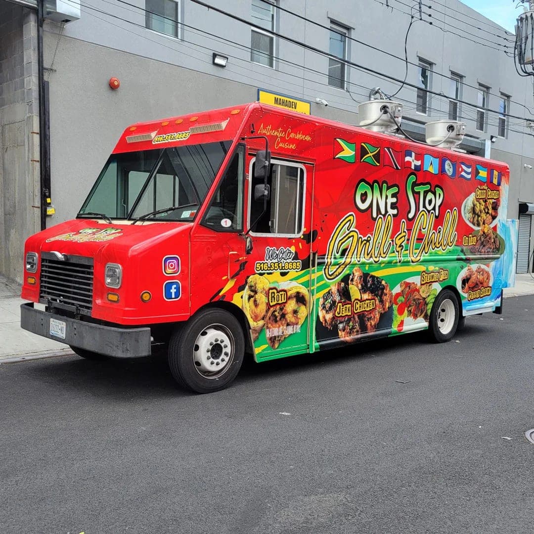 One Stop Grill & Chill Caribbean food truck with a full printed wrap of Caribbean flags and food photos, front three-quarter view outside a brick building