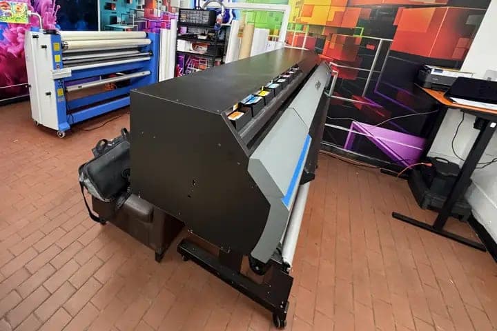 Large-format roll printer in the print room with printed graphics on the wall behind it