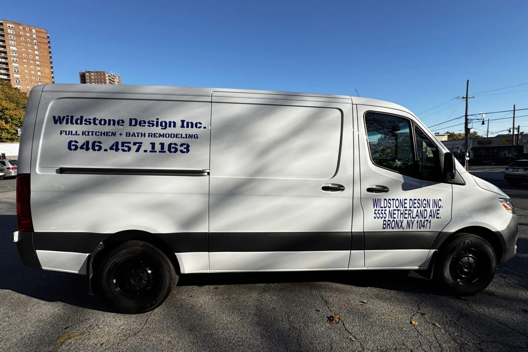 White Mercedes Sprinter for Wildstone Design Inc., a Bronx kitchen-and-bath contractor, with blue cut vinyl lettering and a Netherland Ave, Bronx address on the door, side view outdoors