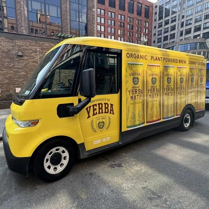 Yellow electric delivery van wrapped with Yerba Maté can graphics, side view on a city street