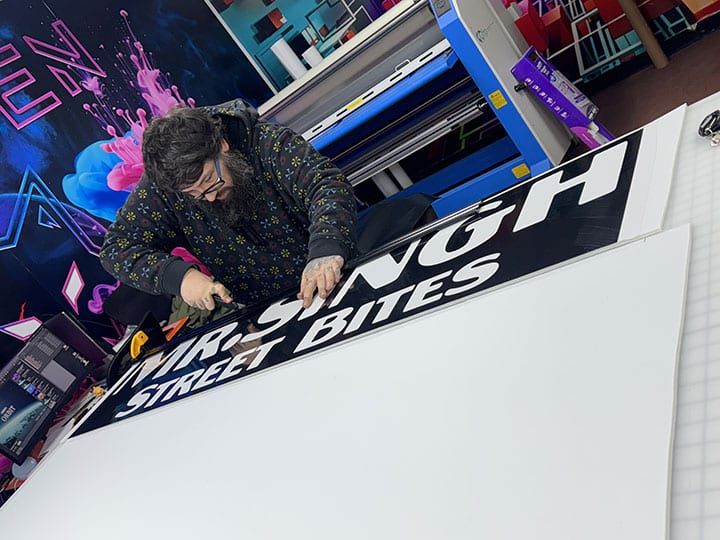 Installer trimming printed lettering for a food cart wrap on the table in the Long Island City shop